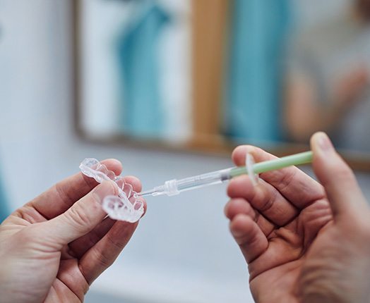 Hands holding a teeth whitening tray and a gel-filled syringe