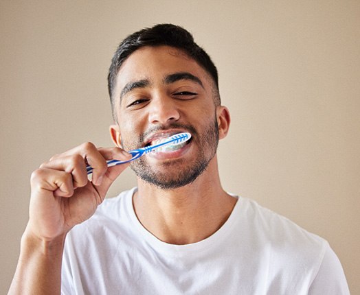 A young man brushing his teeth in front of a bathroom mirror